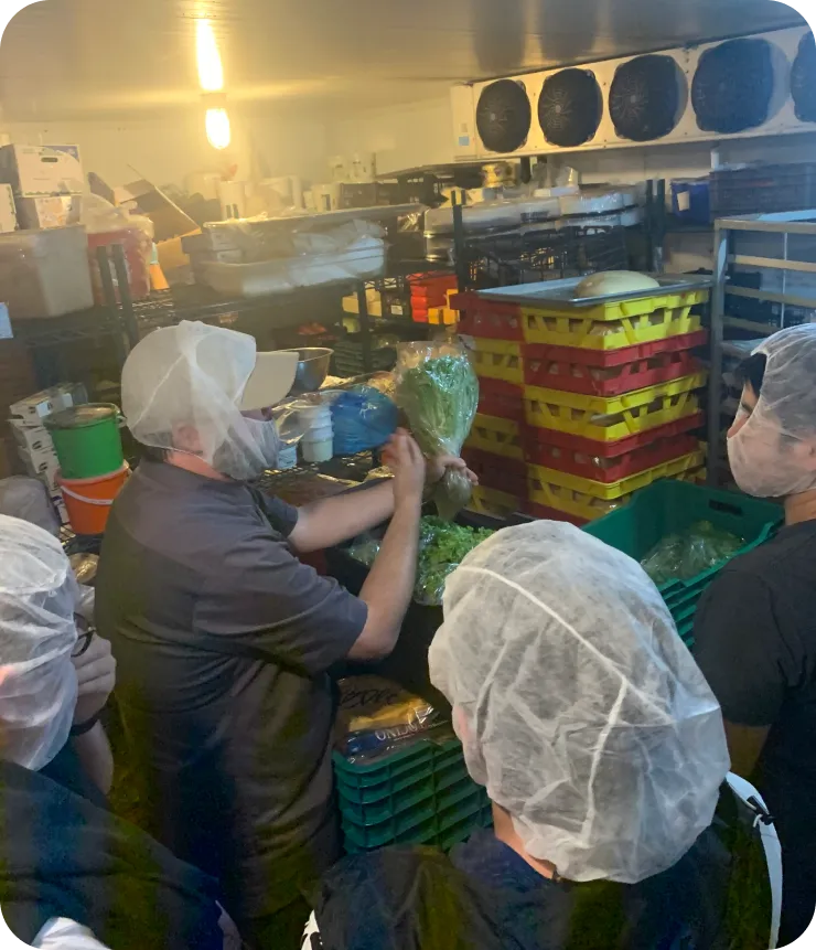 mipOS Dark Kitchen comisariato field research — hair-netted kitchen staff handling fresh produce in yellow and red crates inside a walk-in cooler, informing the inventory-replenishment insights that shaped the product